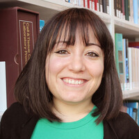 A young woman with brown hair and bangs smiles at the camera.