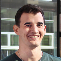 A young white man with short black hair and a green t-shirt smiles at the camera.