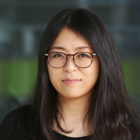 A young Asian woman with long black hair and glasses look at the camera.