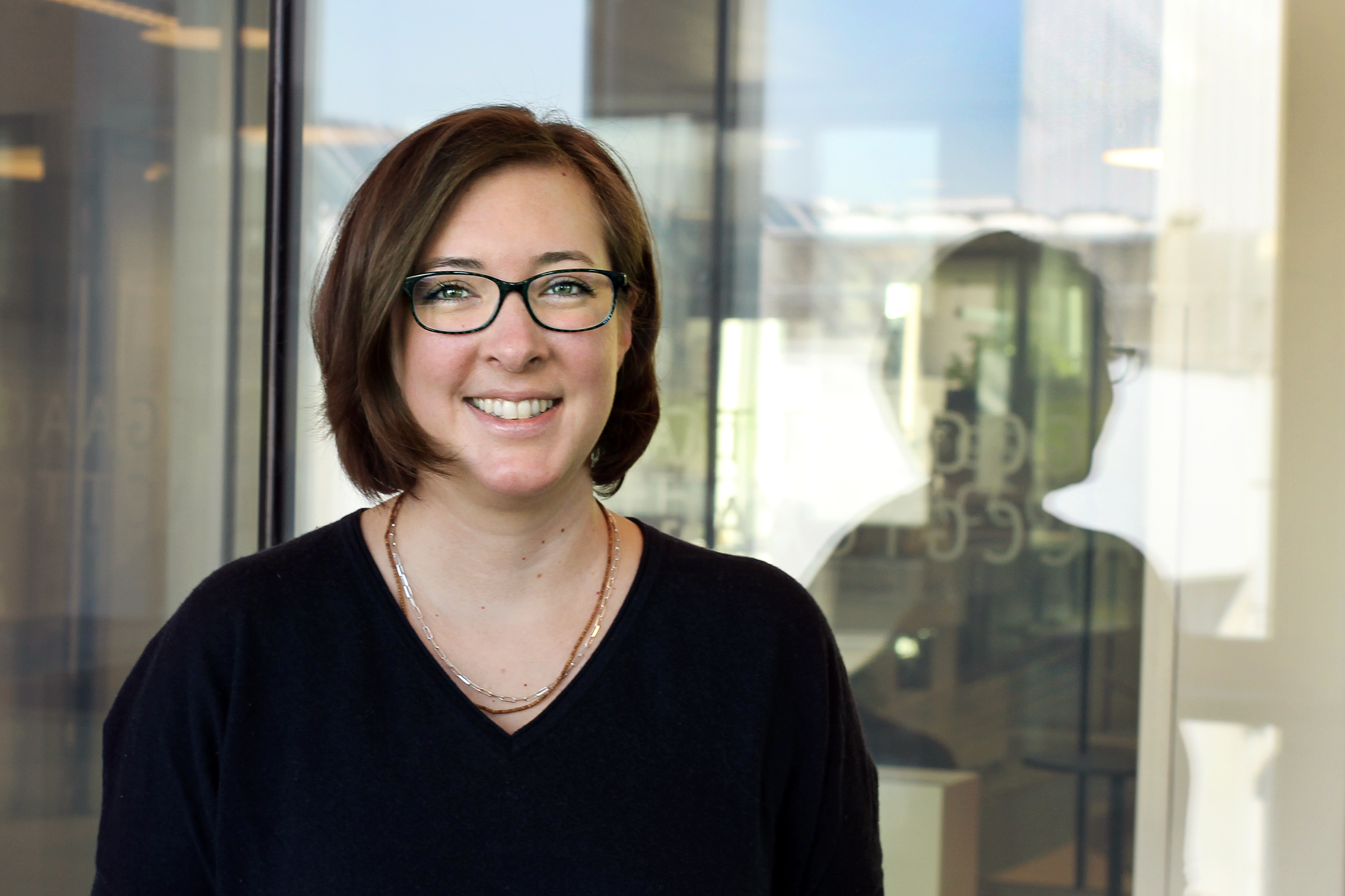 A young woman with short brown hair and glasses smiles at the camera.